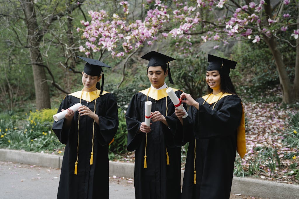 Students in Graduation Gowns and Hats Unfolding Certificates and Magnolia in Background